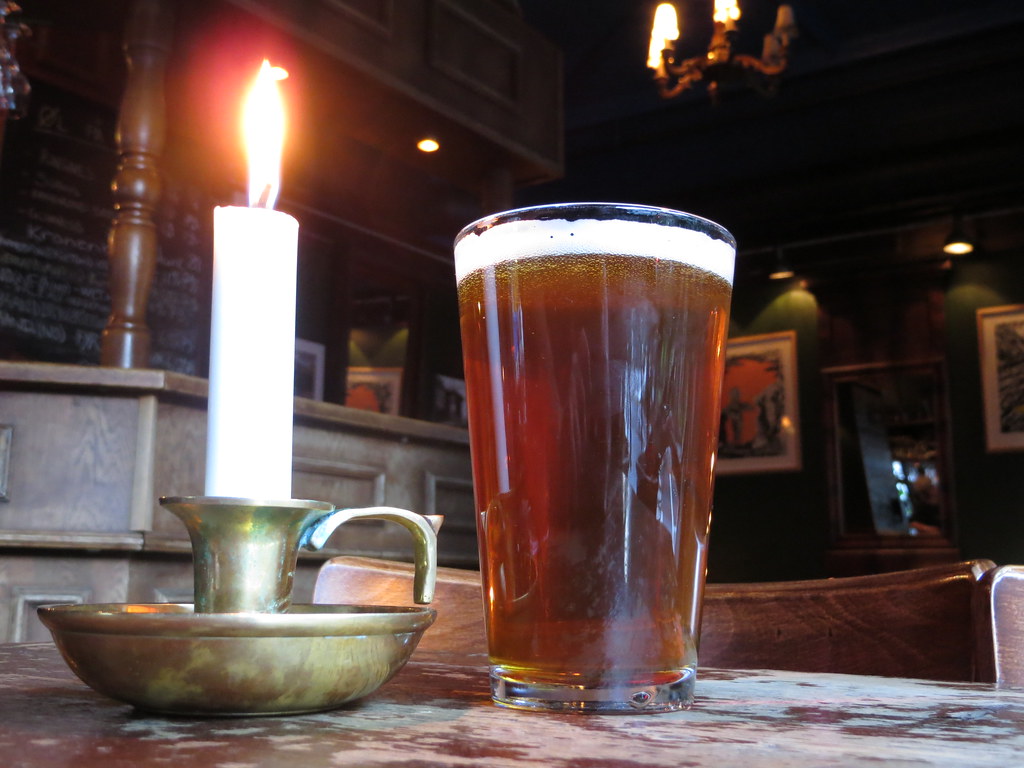 A glass of amber beer on the counter of a cozy pub